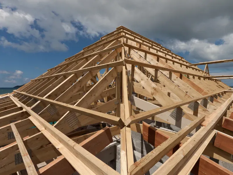 The timber frame of a pitched roof under construction against a blue sky